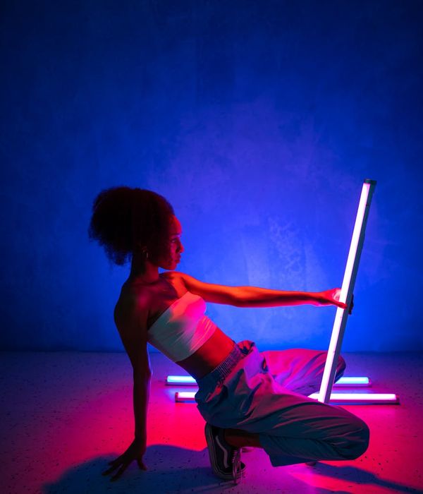 Person in a dynamic movement pose in a dark studio with cyan light trails.